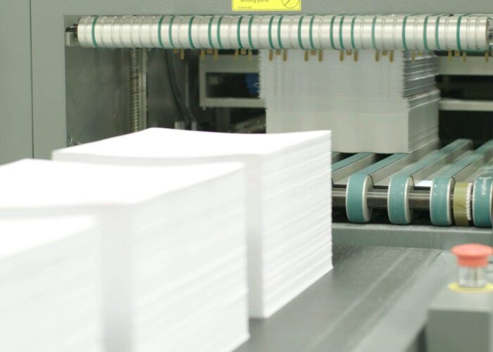 stacks of paper going into a high volume printer.