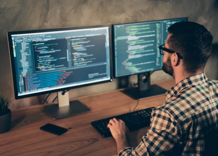 Person coding on two computer monitors.