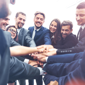 A group of people in suits putting their hands in the middle.