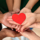 Image: A collection of hands holding a paper cutout heart