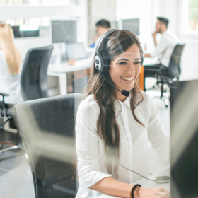 Woman with a headset talking and working on a computer.