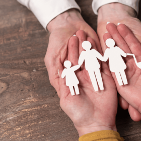 Hands holding a small paper cutout family.